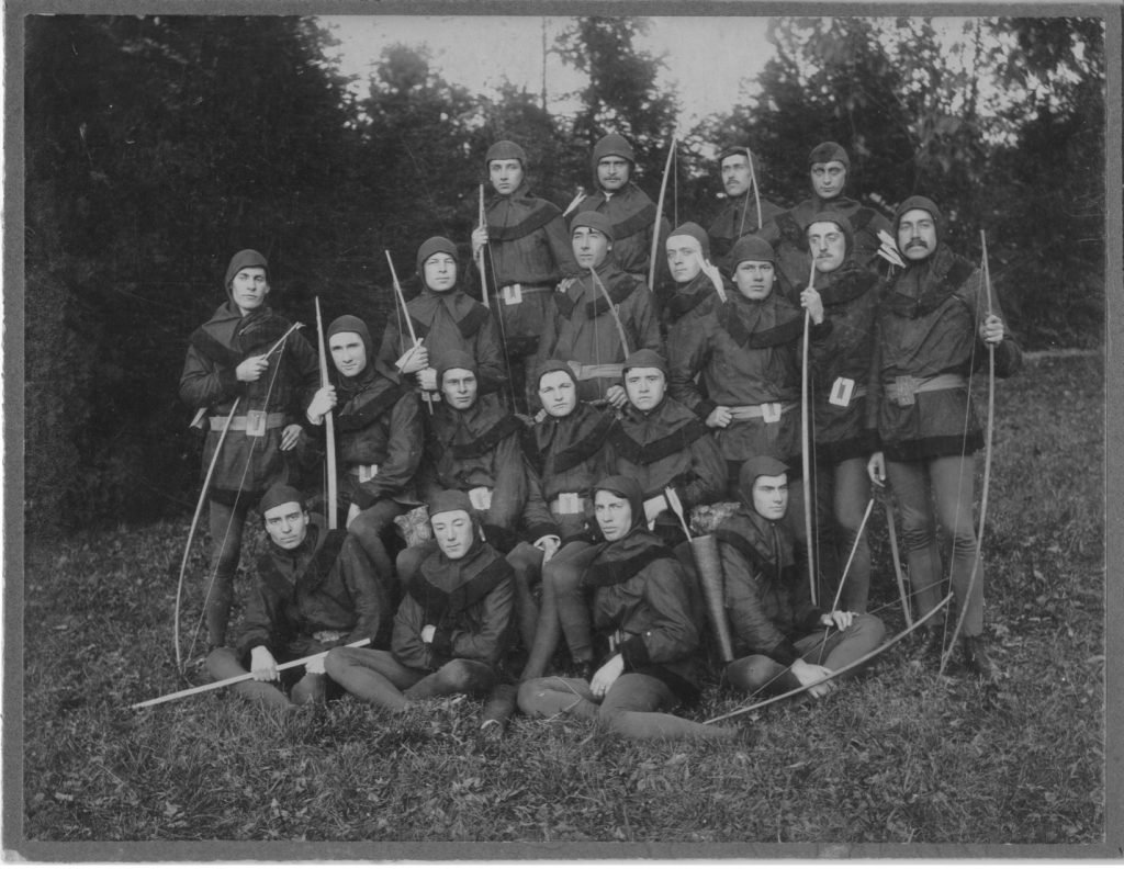 Black and white photo of group of men dressed up in Robin Hood costumes with bow and arrows.